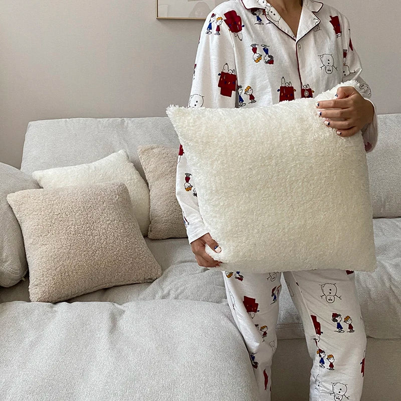 Cream faux fur pillow cover held in front of a sofa (supplier photo)