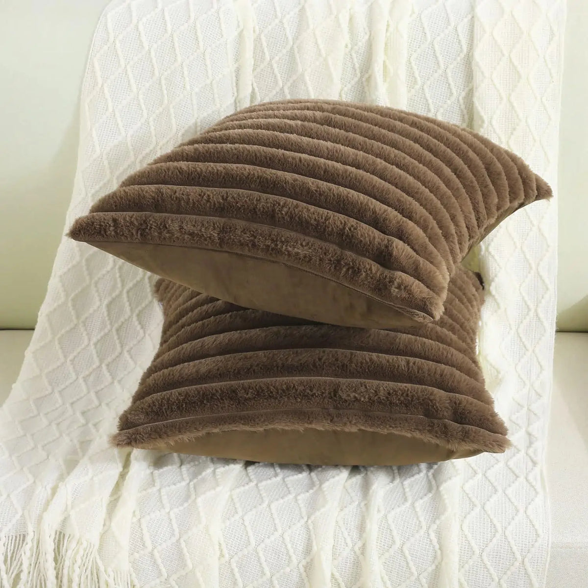 Two dark brown striped faux fur pillow covers stacked on a knit throw