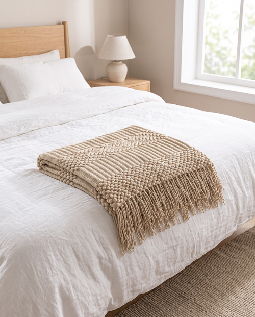 Khaki knitted tassel throw folded across the foot of a bed